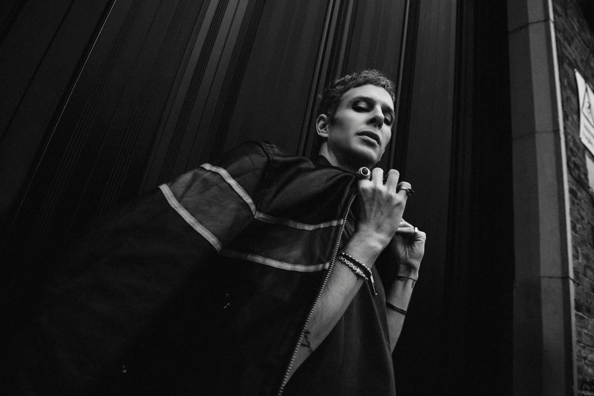 D3LTA in a striped shirt against a dark doorway. Photograph from the Jenny shoot.